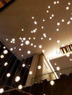 the lights are hanging from the ceiling above the stairs in this modern building, which is decorated with glass balls and wood beams