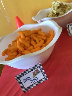 a table topped with bowls filled with cheetos next to cupcakes on top of paper plates