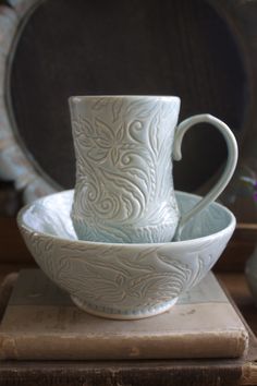 three white cups and saucers sitting on top of a wooden table next to an old book