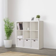 a white bookcase with baskets on the bottom and two plants in front of it