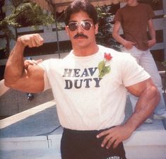 a man with a mustache and sunglasses standing in front of a building, flexing his muscles