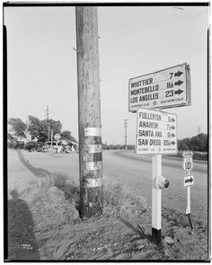 black and white photograph of street signs on the side of the road in front of a telephone pole