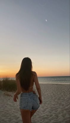 a woman walking on top of a sandy beach next to the ocean under a crescent moon