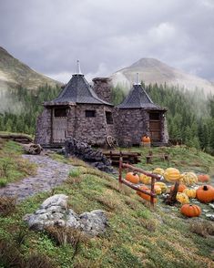 an old stone house with pumpkins in the foreground and mountains in the background