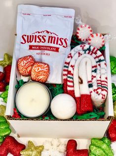 a box filled with assorted holiday treats and candles next to a bag of swiss miss milk