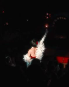 a woman with white feathers on her body in the middle of a crowd at a concert