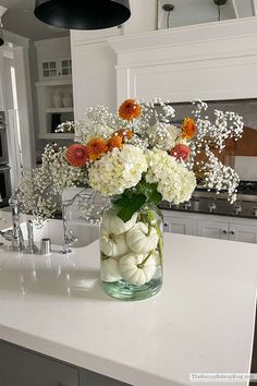 a vase filled with white and orange flowers on top of a kitchen counter next to a sink