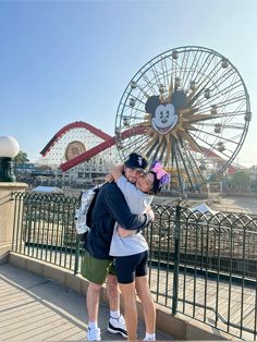 a man and woman hugging each other in front of a ferris wheel at an amusement park