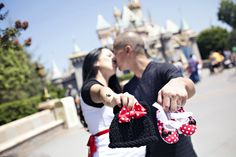 a man and woman kissing in front of a castle with minnie mouse ears on it