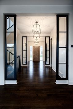 an open door leading to a hallway with wooden floors and black glass panels on the doors