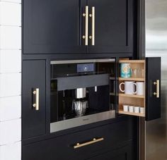 a kitchen with black cabinets and gold pulls on the door, open to reveal a coffee maker