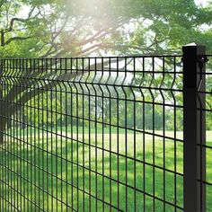 a black wire fence in the middle of a grassy area with trees and grass behind it