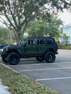 a green jeep parked in a parking lot next to a tree and some cars on the road