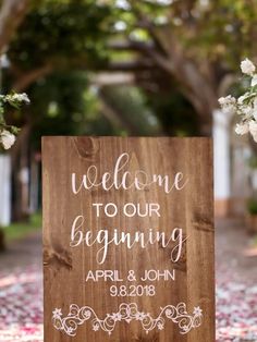 a wooden sign with the words welcome to our beginning on it and flowers in the background