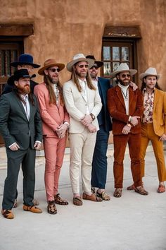 a group of men standing next to each other in front of a brown building wearing suits and hats