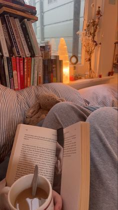 a person sitting on a couch reading a book and holding a cup of coffee in front of them