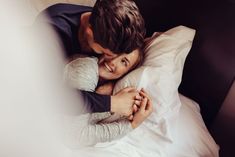 a man and woman cuddling in bed under the covers, smiling at each other