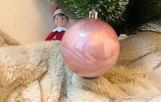 an elf with a pink ornament hanging from a christmas tree on a blanket