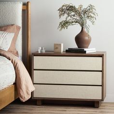 a bedroom with a bed, nightstand and plant on the side table next to it