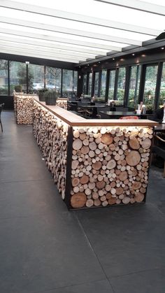 a bar made out of logs in a restaurant with large windows and tables around it