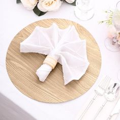 an umbrella shaped napkin sits on top of a wooden plate next to silverware and flowers