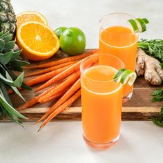 two glasses filled with orange juice next to fresh fruits and vegetables