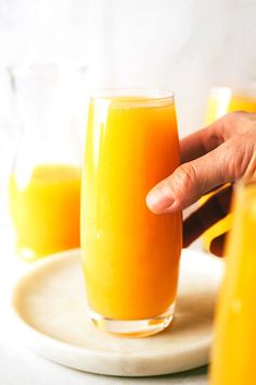 a person is holding a glass of orange juice