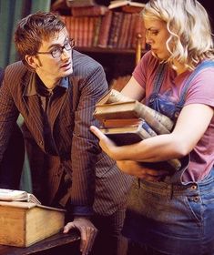 two people standing next to each other in front of a book shelf filled with books