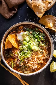 a bowl of mexican soup with tortilla chips and avocado on the side