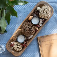 a wooden boat filled with balls and candles on top of a table next to a book