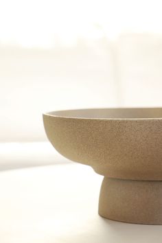 a white bowl sitting on top of a table next to a window with sunlight coming in