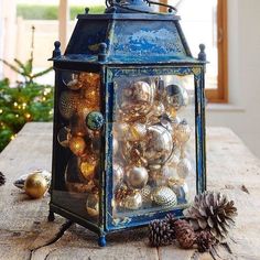 a lantern filled with ornaments on top of a wooden table next to a pine cone