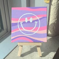 an easel with a painting on it sitting in front of a window that has a smiley face painted on it