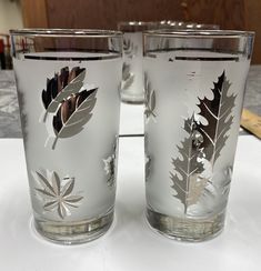 two glasses with leaves on them sitting on a table