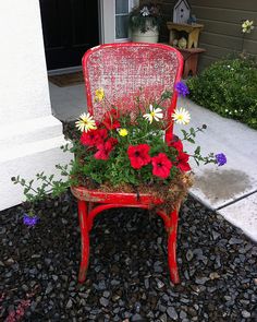 a red chair with flowers in it sitting on gravel