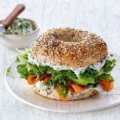 a bagel sandwich sitting on top of a plate next to a bowl of salad