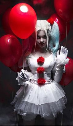 a woman with blue hair and white makeup holding red balloons in front of her face