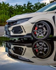 the front end of a white honda civic type car with its reflection in the water