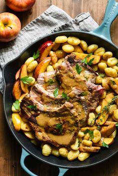 a skillet filled with meat, potatoes and apples on top of a wooden table