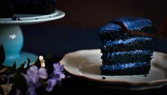 a piece of blue cake sitting on top of a white plate next to a purple flower