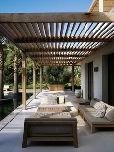 an outdoor living area with couches and tables under a pergolated roof next to a swimming pool