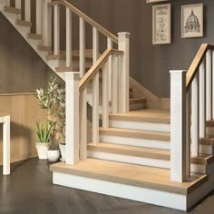 a white staircase with wooden handrails next to potted plants and pictures on the wall