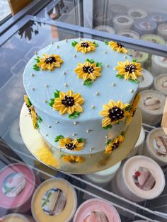 a cake with sunflowers on it sitting in a display case at a bakery