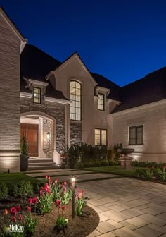 a large house lit up at night with flowers in the front yard