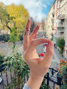 a person's hand with a small tattoo on the middle of their fingers, in front of a city street