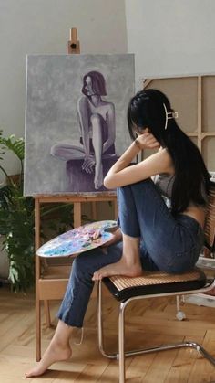 a woman sitting on a chair in front of an easel with a painting behind her