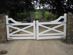 a white gate is open on a dirt road in front of some rocks and trees