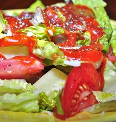 a salad with tomatoes, lettuce and other toppings on a yellow plate