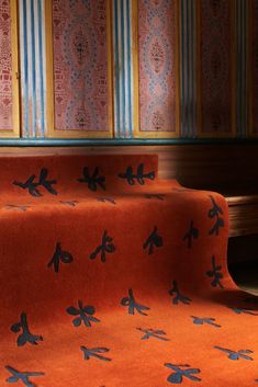 an orange blanket with blue designs on it in front of a wooden bench and colorful wallpaper