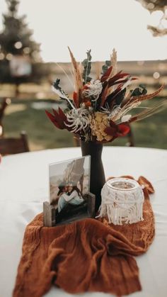 an arrangement of flowers in a vase sitting on top of a white table cloth covered table